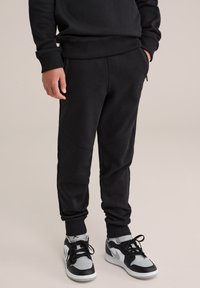 Zwarte sweatpants met een slim fit, gemaakt van zacht katoen. Heeft ribgebreide boorden en zakken. Gecombineerd met zwarte en grijze sneakers.