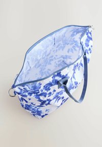 Geantă mare tip tote cu un model floral albastru pe material alb, cu o textură netedă, mânere duble și închidere cu fermoar.