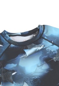 Közelkép egy kék nyakú felsőről, amelyen részletes, foltos ördögráják úsznak a víz alatt.