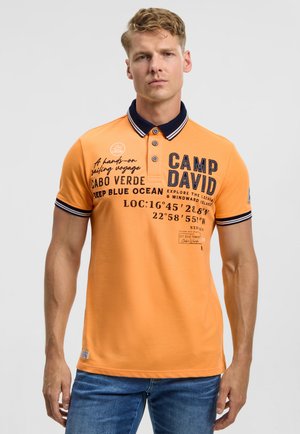 Orangenes Poloshirt mit einem marineblauen Kragen, bedrucktem Text und Grafiken in Dunkelblau. Kurzärmlig, aus Baumwollmaterial, lässiges Design.