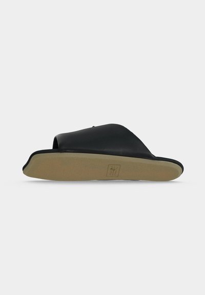 Μαύρο σανδάλι με ανοιχτά δάχτυλα, φαρδιά πάνω λουρίδα και επίπεδη μπεζ σόλα, απεικονιζόμενο από το πλάι σε λευκό φόντο.