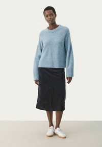 Pull en tricot bleu clair avec un ourlet côtelé, associé à une jupe midi en denim bleu marine foncé avec une fente devant. Des baskets blanches complètent la tenue.