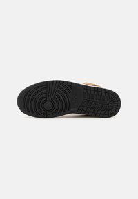 Semelle d'une basket Nike noire avec des motifs d'adhérence circulaires et en grille sur fond blanc.