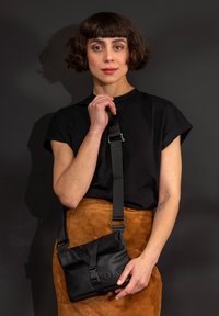 Black crossbody bag with a fold-over flap, adjustable strap, and embossed logo; features a smooth texture and sturdy hardware accents.