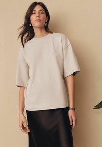 Jasnoszara, oversize koszulka z krótkim rękawem, okrągłym dekoltem i miękką fakturą, zestawiona z czarną satynową spódnicą. Prosty design, minimalne detale.
