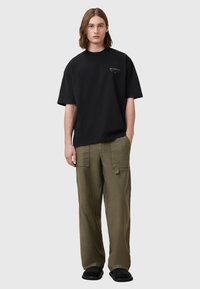Zwarte oversized T-shirt met korte mouwen en een ronde halslijn, gecombineerd met olijfgroene cargobroek en zwarte schoenen.
