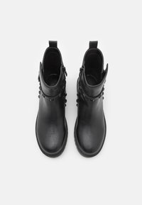 Botas de tobillo negras hechas de cuero sintético texturizado, con un cierre de cremallera y tachuelas decorativas a lo largo de los costados superiores. Acabado suave.