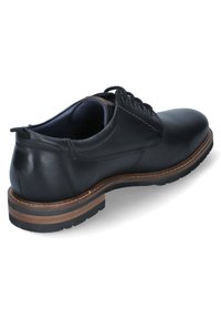 Chaussure en cuir noir avec un bout arrondi, un laçage et une semelle en caoutchouc texturée. Présente un accent marron autour de la semelle.