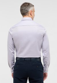 Camicia a maniche lunghe viola chiaro con finitura strutturata, polsini con bottoni e colletto classico, abbinata a pantaloni blu scuro e una cintura nera.