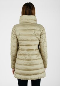 Cappotto imbottito di un beige chiaro con design a righe verticali, colletto alto e lunghezza fino al ginocchio. Materiale liscio e lucido con una leggera lucentezza.