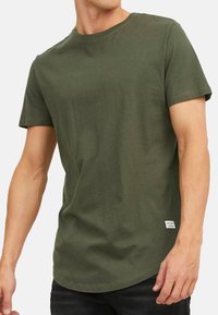 Grøn bomulds T-shirt med korte ærmer, rund hals og lige kant. Har et lille mærke i nederste venstre side.