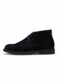 Stivaletti alla caviglia in suede nero con punta tonda, lacci sottili e suola in gomma nera texturizzata. Presentano un design elegante e minimalista.