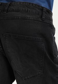 Jeans de mezclilla negra con una textura suave, que cuentan con un bolsillo trasero, pasadores para cinturón y un diseño de cintura alta.