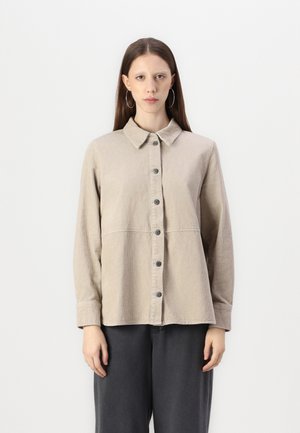 Beige corduroy shirt with a collared neckline, buttoned front, long sleeves, and a horizontal seam across the torso. Textured fabric.