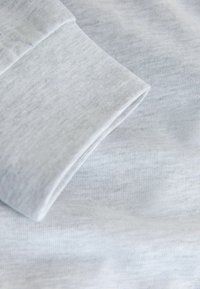 Světlé šedé bavlněné plátno s hladkou texturou, které ukazuje otočený manžet a jemný horizontální úplet. Jednoduchý a minimalistický design.