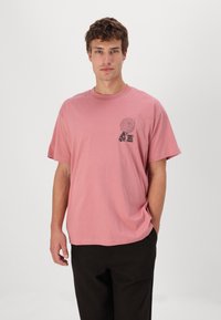 Roze katoenen T-shirt met korte mouwen, voorzien van een grafische print op de linkerkant van de borst. Losse pasvorm met een ronde hals.