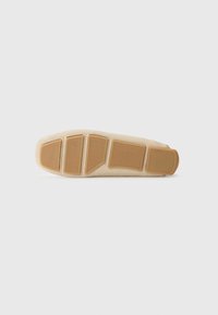 Footwear with a beige upper and a gum rubber sole. The sole features distinctive cut-outs and a textured pattern for traction.