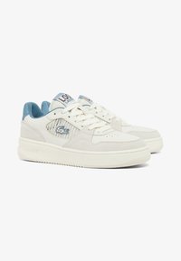 Baskets Lacoste en cuir blanc cassé avec des accents bleu clair, dotées d'une couche en daim, d'une fermeture à lacets et d'une semelle en caoutchouc texturée.