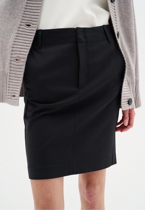 Jupe crayon noire à la texture lisse, dotée de poches à l'avant et d'une silhouette ajustée, associée à un cardigan gris clair.