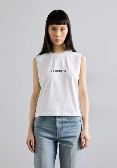 T-shirt en coton blanc sans manches avec un col rond et le texte "SOIS HONTEUX" imprimé en noir sur le devant. Associé à un jean bleu clair.