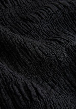 Sort tekstureret stof med en bølget overflade. Materialet virker blødt og elastisk og skaber en lagdelt effekt med varierende dybder.