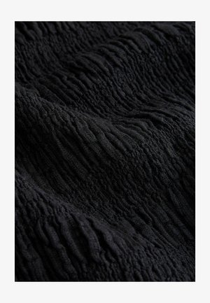 Sort tekstureret stof med en bølget overflade. Materialet virker blødt og elastisk og skaber en lagdelt effekt med varierende dybder.