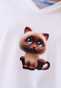 Biała koszulka z nadrukiem rysunkowego kociaka z dużymi niebieskimi oczami, jasnym futrem i brązowymi akcentami, siedzącego w zabawnej pozie.
