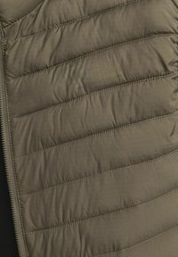 Olivengrünes Puffer-Westen mit gestepptem Muster, ausgestattet mit vertikalen Nähten und einem silbernen Reißverschluss. Weiche, leichte und glatte Textur.