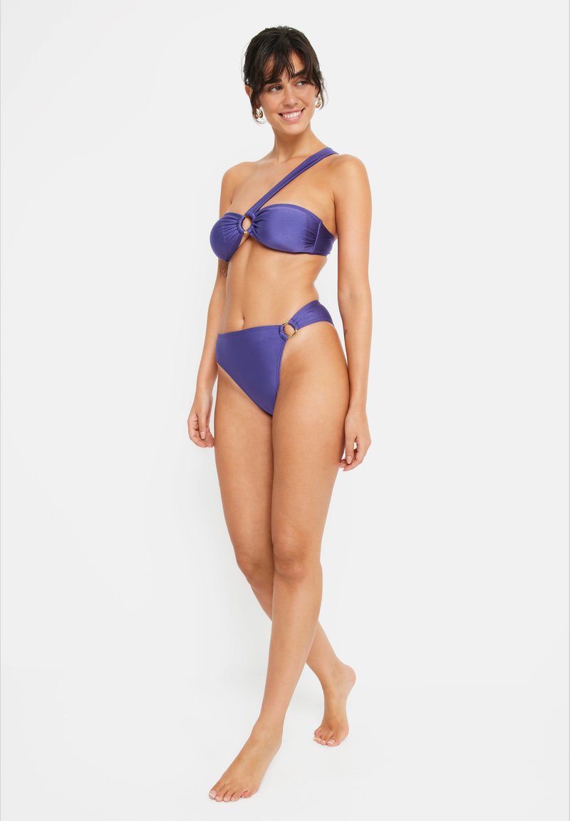 Purple bikini set with a one-shoulder bandeau top featuring a circular accent, and matching high-waisted bottoms with side rings. Smooth texture.