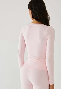 Top z długim rękawem i legginsy z miękkiego różowego materiału, charakteryzujące się dopasowanym krojem i subtelnym logo z tyłu. Gładka faktura na całej powierzchni.