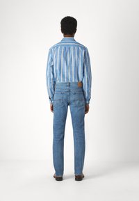 Camicia a righe verticali blu chiaro con colletto, abbinata a jeans in denim blu chiaro con una tasca posteriore decorativa e etichetta marrone.