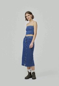 Denim crop top i suknja visokog struka u srednje plavoj boji, s ravnim siluetom, prednjim prorezom i uparenim s smeškim čizmama do gležnja.