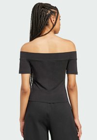 Mustat olkaimeton paita lyhyillä hihoilla, tiukka malli, pehmeä rakenne ja minimaaliset saumat. Yhdistetty tummiin housuihin.