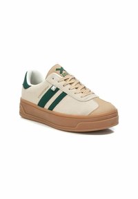 Zapatillas de ante beige con rayas verdes, forro de malla blanca y suela de goma marrón. Cuenta con cordones y detalles de marca en la lengüeta.
