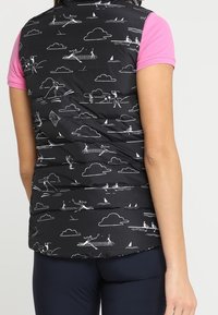 Svart pufferväst med vita sportinspirerade illustrationer, med hög krage och korta ärmar i rosa, kombinerad med marinblå byxor.