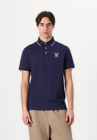 Laivyno mėlynos spalvos polo marškiniai su baltais apykaklės ir rankovių akcentais, su mažuoju logotipu kairėje krūtinės pusėje. Pagaminti iš tekstūruoto audinio.