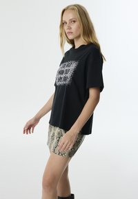 Camiseta negra de manga corta con un diseño gráfico, combinada con una falda mini ajustada con estampado de serpiente. Textura de tela suave.