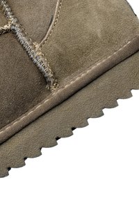 Bota de tobillo de ante marrón con una superficie texturada, costuras en contraste y una suela de goma que presenta un patrón de zigzag.