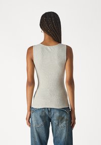 Top tipo tank gris con cuello redondo, combinado con jeans de mezclilla azul de corte amplio que presentan detalles bordados en los bolsillos traseros.