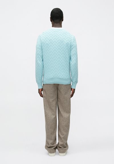 Pull bleu clair texturé avec un col blanc, associé à un pantalon marron ample. Le tissu semble doux avec un motif de tricot visible.