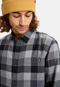 Gray and black plaid flannel shirt with yellow accents, button closure, and left chest pocket featuring a logo patch. Wool blend material.