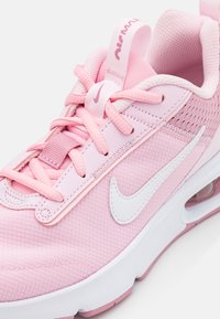 Rosa Nike-sneakers med nettingoverdel, hvite detaljer og en teksturert overflate. Sålen er hvit med en synlig luftenhet.