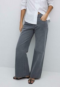 Weite graue Jeans aus Denim mit hoher Taille, klassischem 5-Taschen-Design und minimalen Nähdetails, kombiniert mit einem weißen Hemd.
