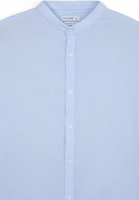 Camicia azzurro chiaro con colletto alla band, realizzata in tessuto testurizzato. Presenta una patta centrale con bottoni e un design confortevole.