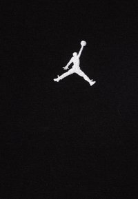 Tessuto nero con una texture morbida presenta un logo Jumpman ricamato in bianco, che rappresenta una figura in una posa dinamica che tiene un pallone da basket.