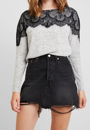 Vrouw draagt een grijze trui met zwarte kanten accenten over de schouders en een zwarte denim minirok met distressed details.