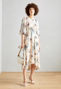 Floral midi dress in pastel colors with bell sleeves, gathered waist, and asymmetric hem. Paired with strappy heels and a small handbag.