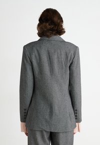 Grijze op maat gemaakte blazer met een gestructureerde pasvorm, notch revers en vierknoppige manchetten. Heeft een subtiele textuurstof en een enkele achterste split.