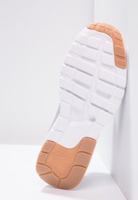 Nike sneakersula, med en vit gummibas och texturerade sulmönster samt en orange accent vid hälen. Hållbar och funktionell design.