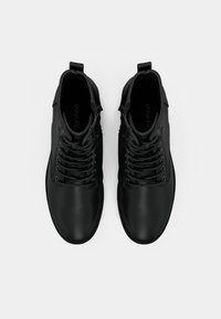 Paire de bottines noires en cuir à lacets avec languettes de tirage, vue de dessus sur fond blanc.